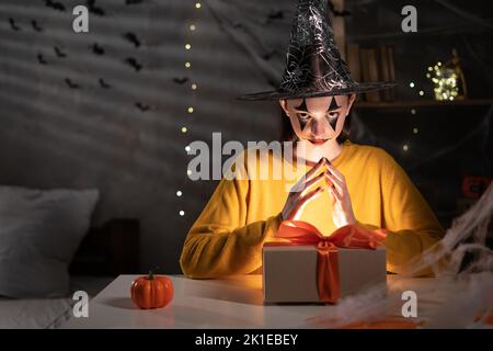 Halloween fille avec clown maquillage assis à la table dans la pièce sombre boîte de maintien avec lanterne, Halloween vente concept Banque D'Images