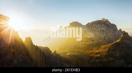 Vue d'en haut, vue aérienne stupéfiante d'une chaîne de montagnes pendant un beau lever de soleil avec une cabane de montagne au loin. Banque D'Images