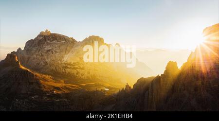 Vue d'en haut, vue aérienne stupéfiante d'une chaîne de montagnes pendant un beau lever de soleil avec une cabane de montagne au loin. Banque D'Images