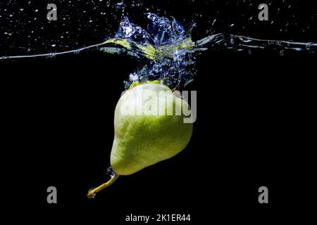 Poire verte entière tombée dans l'eau avec des éclaboussures isolées sur fond noir. Banque D'Images