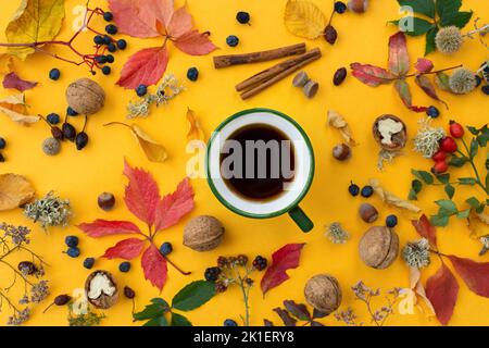 Composition de l'automne vue du dessus. Une couche uniforme de noix, de feuilles, de baies, de fleurs d'automne sur fond orange vif avec une tasse de café vert au centre Banque D'Images