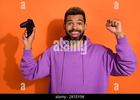 Photo de garçon positif bonbon homme profiter du jeu de réussite de gain tenir les mains vers le haut playstation isolé sur fond de couleur orange Banque D'Images