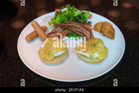 Œuf benedict isolé sur une assiette avec salade et saucisse et sauce hollandaise à la crème Banque D'Images