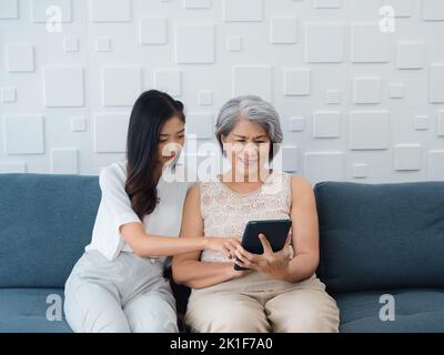 Bonne belle femme asiatique senior, mère cheveux blancs et jolie jeune femme, fille pointant et regardant l'écran de tablette numérique, profitez de regarder vid Banque D'Images