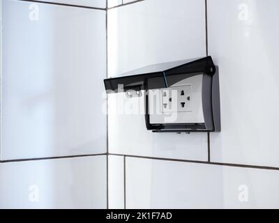 Panneau de prise électrique blanc à fiche en gros plan avec écran en plastique transparent sur les carreaux du mur de la salle de bains. Prise femelle avec coque de protection Waterp Banque D'Images