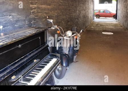 Un piano noir vintage avec un cyclomoteur noir rétro dans l'arcade d'une maison par un beau jour. Copier l'espace. Banque D'Images