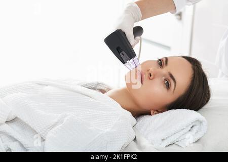 Femme pendant la procédure de levage RF pour sa peau de visage serrer avec cosmetologiste dans un salon de beauté Banque D'Images