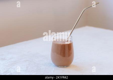 Smoothie au chocolat aux protéines sain avec paille métallique sur table blanche, gros plan. Banque D'Images