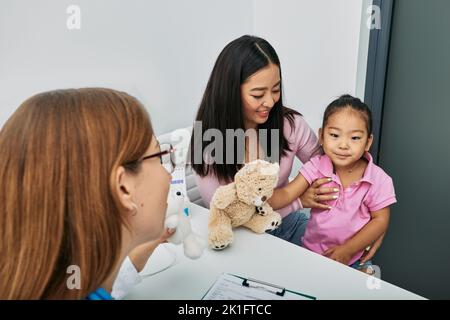 Le médecin communique avec la petite patiente asiatique lors de sa visite à la clinique médicale avec sa mère. Santé des enfants Banque D'Images