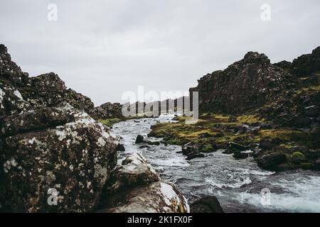 Un ruisseau de montagne d'eau froide sombre près de la cascade d'Oxararfoss dans le parc national de Thingvellir, en Islande. Herbe verte au milieu des rochers sous le son Banque D'Images