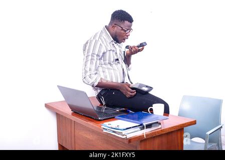 jeune homme d'affaires au bureau, portant des lunettes optiques parlant sur le haut-parleur du combiné de téléphone portable. Banque D'Images