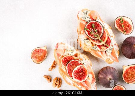 Bruschetta croissant frais avec figue mûre, fromage bleu, prosciutto, noix et herbes sur fond de table en béton blanc avec espace de copie. Vue de dessus, s Banque D'Images