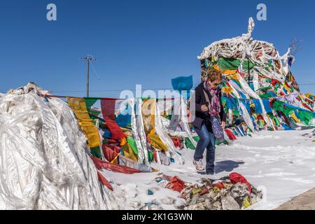 Une Dame vient d'attacher un châle de prière à côté des drapeaux de prière au lac Yamdrok au Tibet en Chine Banque D'Images