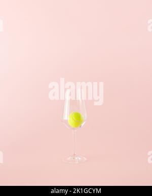 Yellow tennis ball in a transparent drinking glass on a pink background. Minimal concept. Banque D'Images
