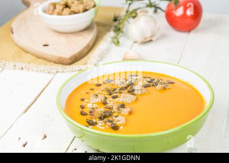 Soupe à la crème végétalienne mélangée à base de tomates fraîches. Sur une table en bois blanc. Soupe de carottes aux tomates avec des croûtons et des graines de citrouille. Banque D'Images