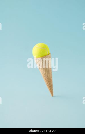 Cône de glace avec balle de tennis jaune sur fond bleu flottant. Concept minimal. Banque D'Images