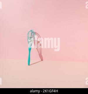 Turquoise egg mixer beater, manual cream mixing whisk with disco ball leaning on pink background. Minimal concept. Stock Photo