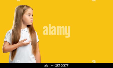 Enfant confus. Contexte promotionnel. Offre spéciale. Portrait d'une petite fille perplexe et réfléchie regardant invisible texte d'information sur le produit isolat Banque D'Images