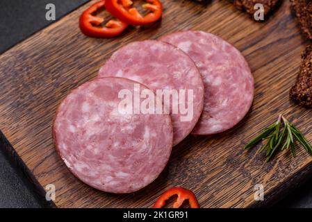 Délicieux saucisses fumées fraîches coupées avec des tranches sur une planche à découper en bois sur fond de béton foncé Banque D'Images