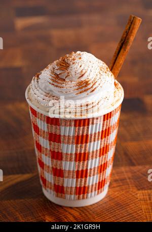 Un Latte à la citrouille épicée recouvert de crème fouettée dans une tasse jetable sur une table en bois Banque D'Images