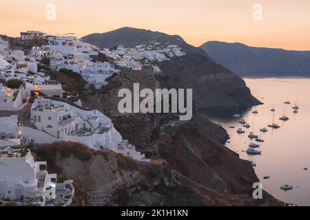 Le village perché d'Oia au sommet d'une spectaculaire côte de roche volcanique au-dessus de la mer Égée au coucher du soleil ou au lever du soleil sur l'île grecque de Santorini, en Grèce. Banque D'Images