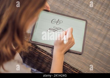 Calligraphe la jeune femme écrit une phrase sur une tablette numérique. Inscription de lettres ornementales. Calligraphie, graphisme, lettrage, écriture manuscrite Banque D'Images