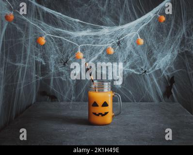 Boisson d'Halloween avec visage de citrouille ou de lanterne. Cocktail de citrouille dans un pot en verre sur fond bleu foncé. Décorations pour la fête des enfants. Copier l'espace. Banque D'Images