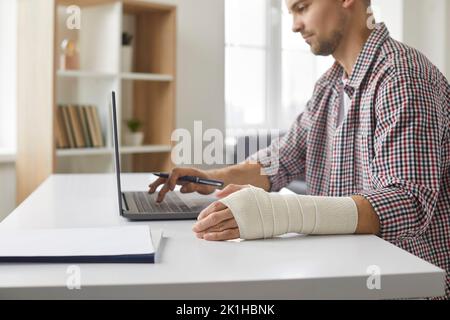 Un jeune homme concentré avec un ligament tentaculaire dans son bras travaille sur un ordinateur portable dans son bureau. Banque D'Images