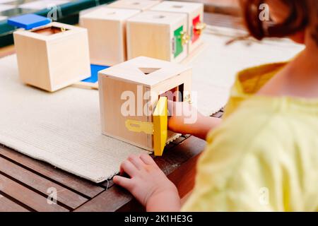 Petite fille joue avec un matériel éducatif montessori pour ouvrir et fermer des boîtes en bois. Banque D'Images