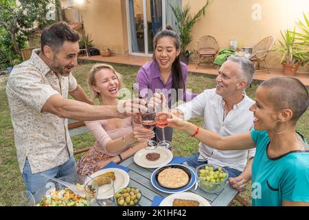 Des amis multiraciaux dégustent et dégustent du vin autour de la table au restaurant sur le patio de la maison. Banque D'Images