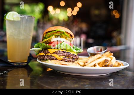 cheeseburger avec deux viandes, des cornichons et des frites sur un bar Banque D'Images