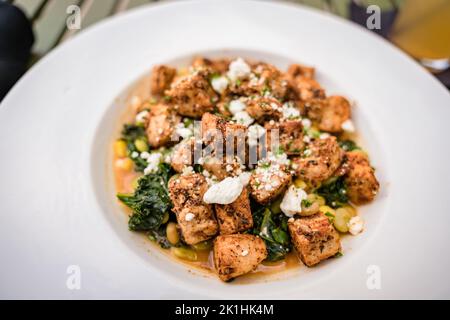 plat de poulet sauté recouvert de feta et accompagné d'épinards sautés dans un bol de service blanc Banque D'Images