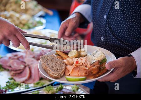 Homme senior tenant une assiette avec une sélection de morceaux de froid, pain et salade, servi une tranche de viande au buffet, homme choisissant la nourriture Banque D'Images