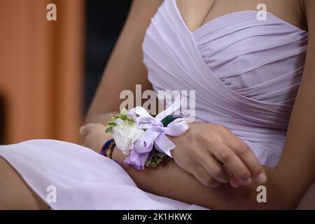 Gros plan d'une jeune femme caucasienne vêtue de soie mauve clair, assise à une cérémonie de mariage et tenant les doigts dans un geste nerveux Banque D'Images