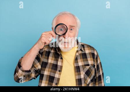 Photo de l'homme funky impressionné retraité vêtu chemise à carreaux qui a l'air d'agrandir verre isolé couleur bleue fond Banque D'Images