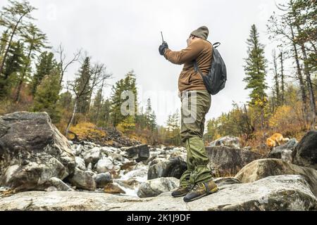 Un touriste-voyageur avec un sac à dos se tient devant une rivière de montagne dans une forêt d'automne. Le concept de liberté et d'unité avec la nature Banque D'Images