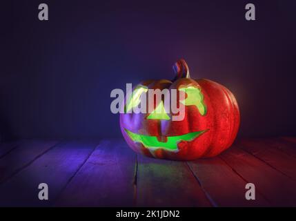 Citrouille d'Halloween sur un bureau en bois sur le fond d'un mur sombre. Banque D'Images