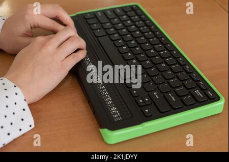 Une femme aveugle utilise un ordinateur avec un écran en braille et un clavier d'ordinateur. Périphérique inclus. Banque D'Images