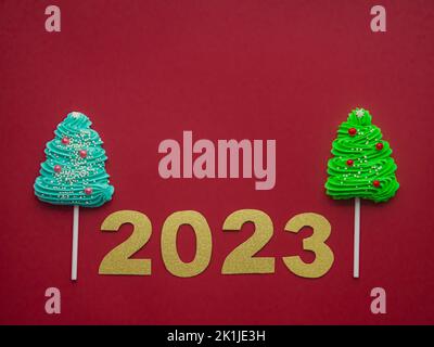 2023 et des bonbons verts et bleus sous forme d'arbre de Noël sur fond rouge Banque D'Images