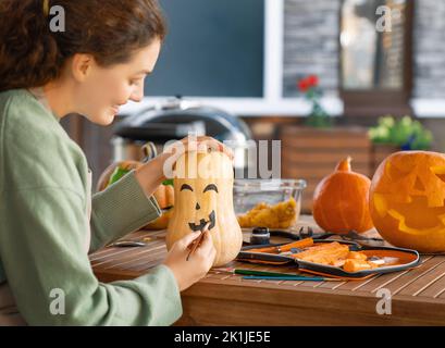 Une femme heureuse est en train de sculpter une grande citrouille d'orange pour la fête d'Halloween. Banque D'Images