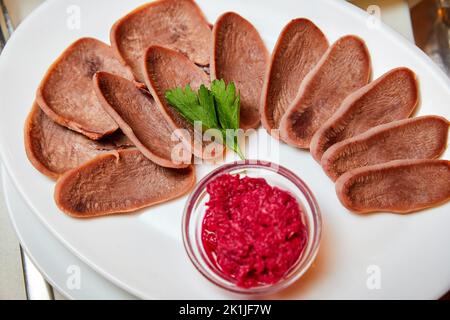 La langue de bœuf coupée avec du raifort et des herbes sur une assiette blanche Banque D'Images