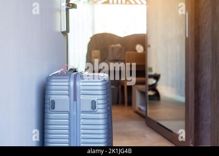 Bagages gris dans une chambre d'hôtel moderne après ouverture de la porte. Concepts de temps de voyage, de voyage, de voyage et de vacances Banque D'Images