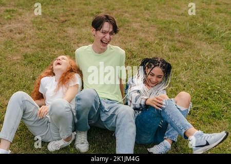 Heureux jeunes trois meilleurs amis s'amuser ensemble en plein air assis sur l'herbe dans le parc public de la ville. Concept d'amitié féminine. Concept de gentillesse Banque D'Images