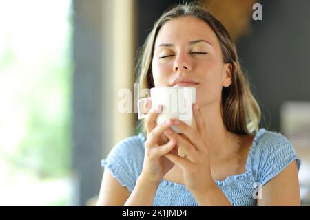 Une jeune femme sent l'arôme du café dans une tasse dans un restaurant Banque D'Images