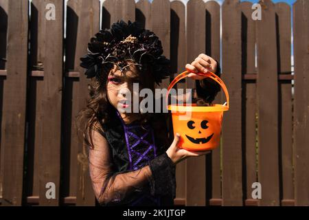 fille en costume de sorcière tenant le seau d'halloween et regardant l'appareil photo avec la grimace en colère Banque D'Images