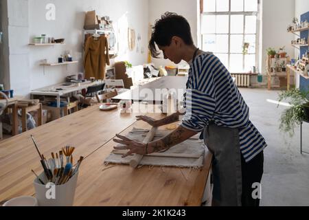 Jeune femme italienne concentrée propriétaire de petite entreprise roulant avec de l'argile brute de pin à la table Banque D'Images