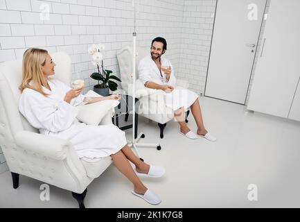 Beau homme avec sa petite amie avec des verres de boisson rafraîchissante au citron dans le centre de bien-être. Couple pendant la thérapie de vitamine intraveineuse. Détox orga humaine Banque D'Images