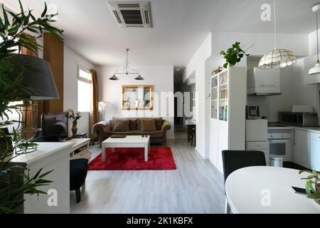 Ce studio comprend une petite cuisine ouverte blanche et une table ronde en bois blanc avec des chaises capitonnées noires et une sof de chesterfield marron Banque D'Images