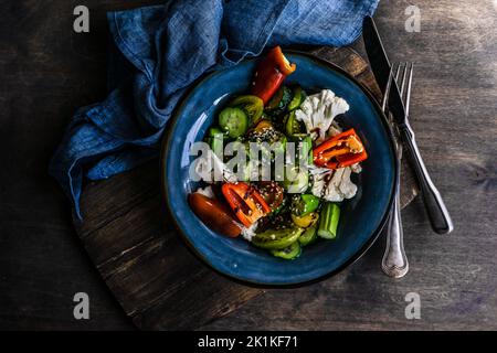 Vue en hauteur d'un bol d'okra, chou-fleur, concombre, poivron rouge, tomate et salade de sésame avec sauce soja Banque D'Images