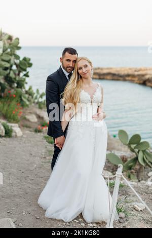 Portrait de couple de mariage debout près des feuilles de cactus d'opuntia. Jeunes mariés se marient les mains avec le marié en costume. Banque D'Images